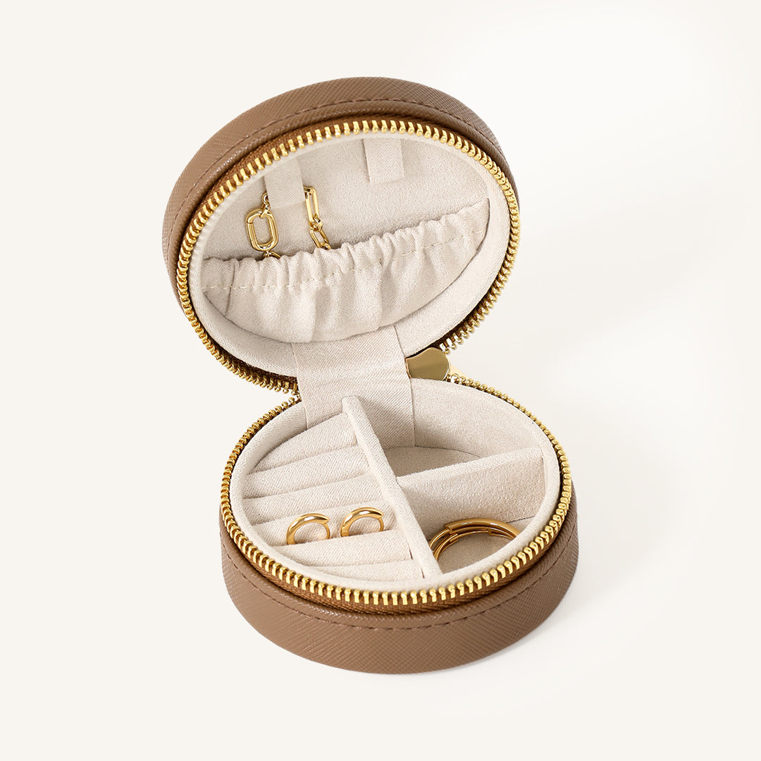 A compact round Sienna Jewellery Box made of Brown Vegan saffiano leather, opened to display its interior compartments where jewellery items like earrings are stored.