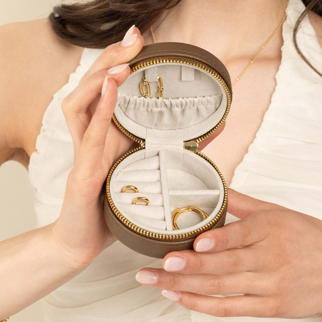 A compact round Sienna Jewellery Box made of Brown Vegan saffiano leather, opened to display its interior compartments where jewellery items like earrings are stored.