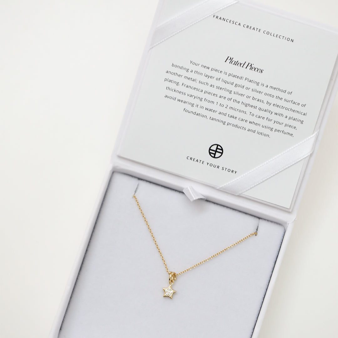 A gold necklace featuring a star-shaped charm pendant with cubic zirconias in the centre attached to gold chain, displayed in white box