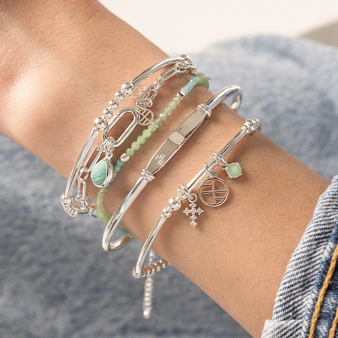 A petite silver cross charm with cubic zirconia attached to bracelet on wrist