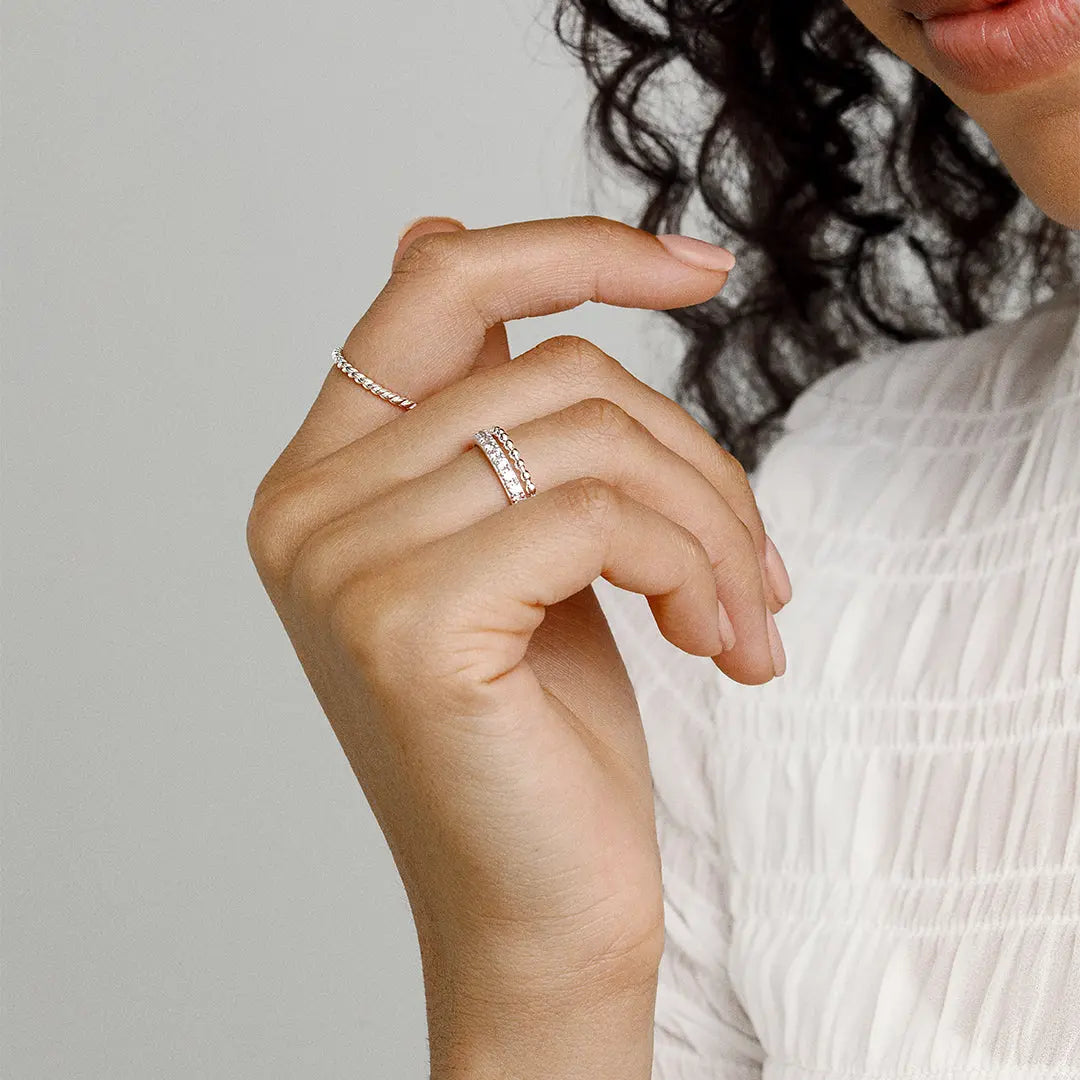 A silver coloured stacking ring with a simple, elegant design featuring small, uniform beads around its circumference worn on finger