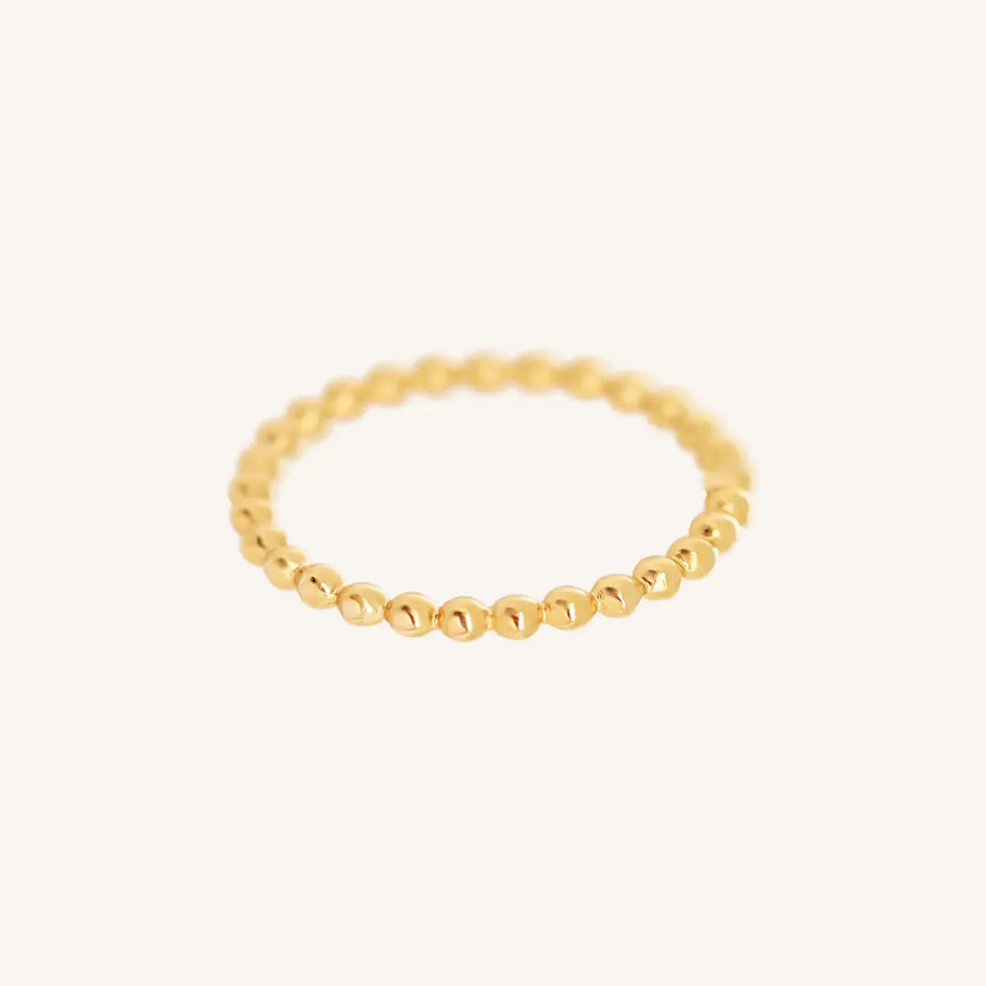A gold coloured stacking ring with a simple, elegant design featuring small, uniform beads around its circumference.
