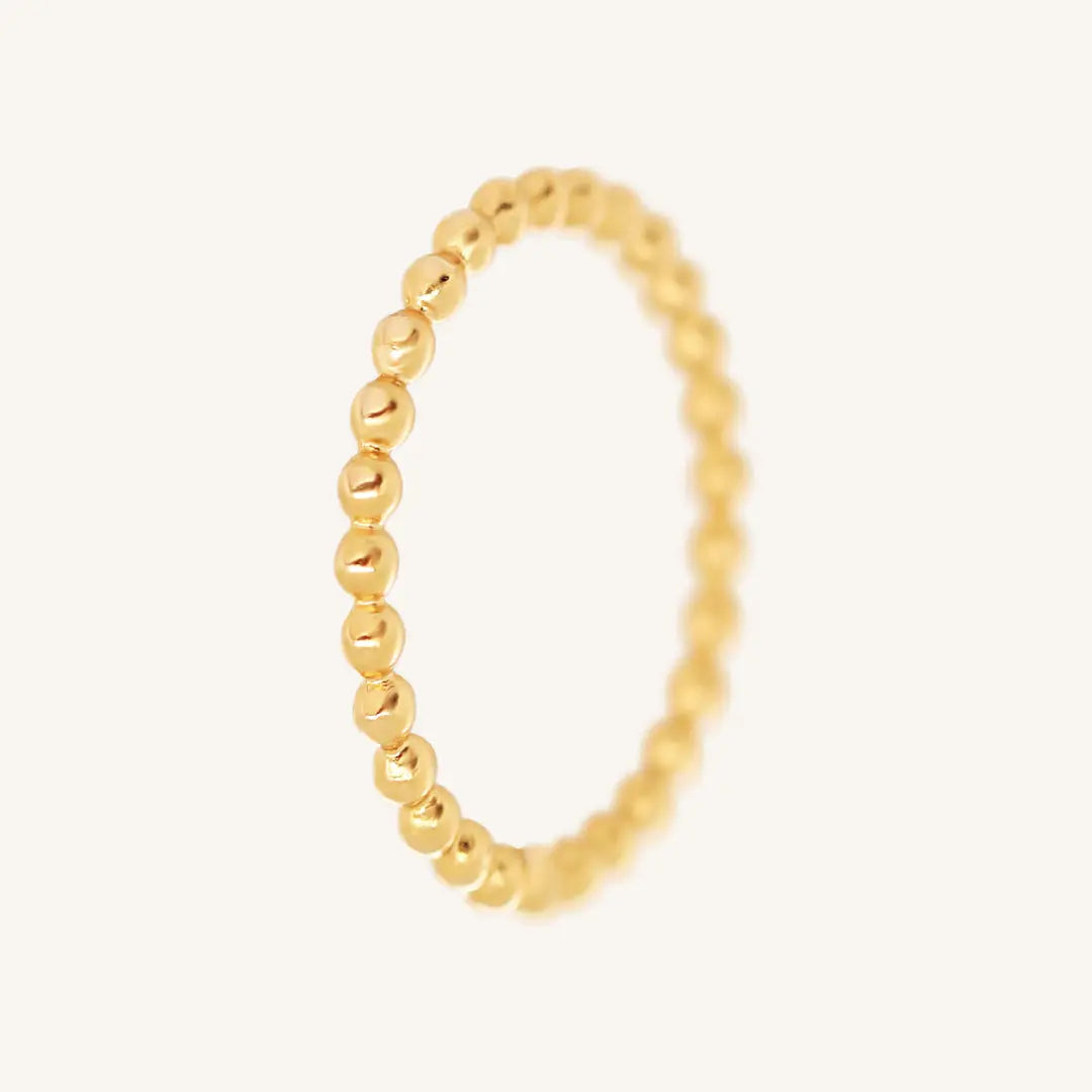 A gold coloured stacking ring with a simple, elegant design featuring small, uniform beads around its circumference.