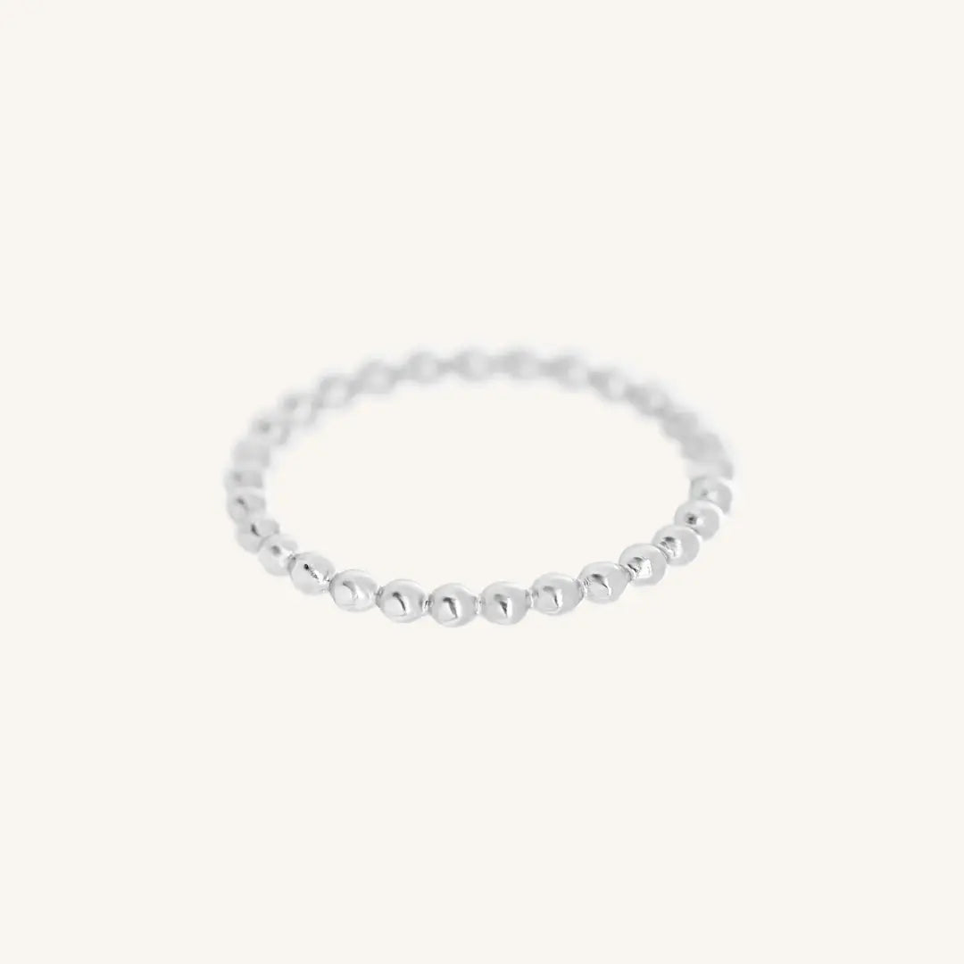 A silver coloured stacking ring with a simple, elegant design featuring small, uniform beads around its circumference.