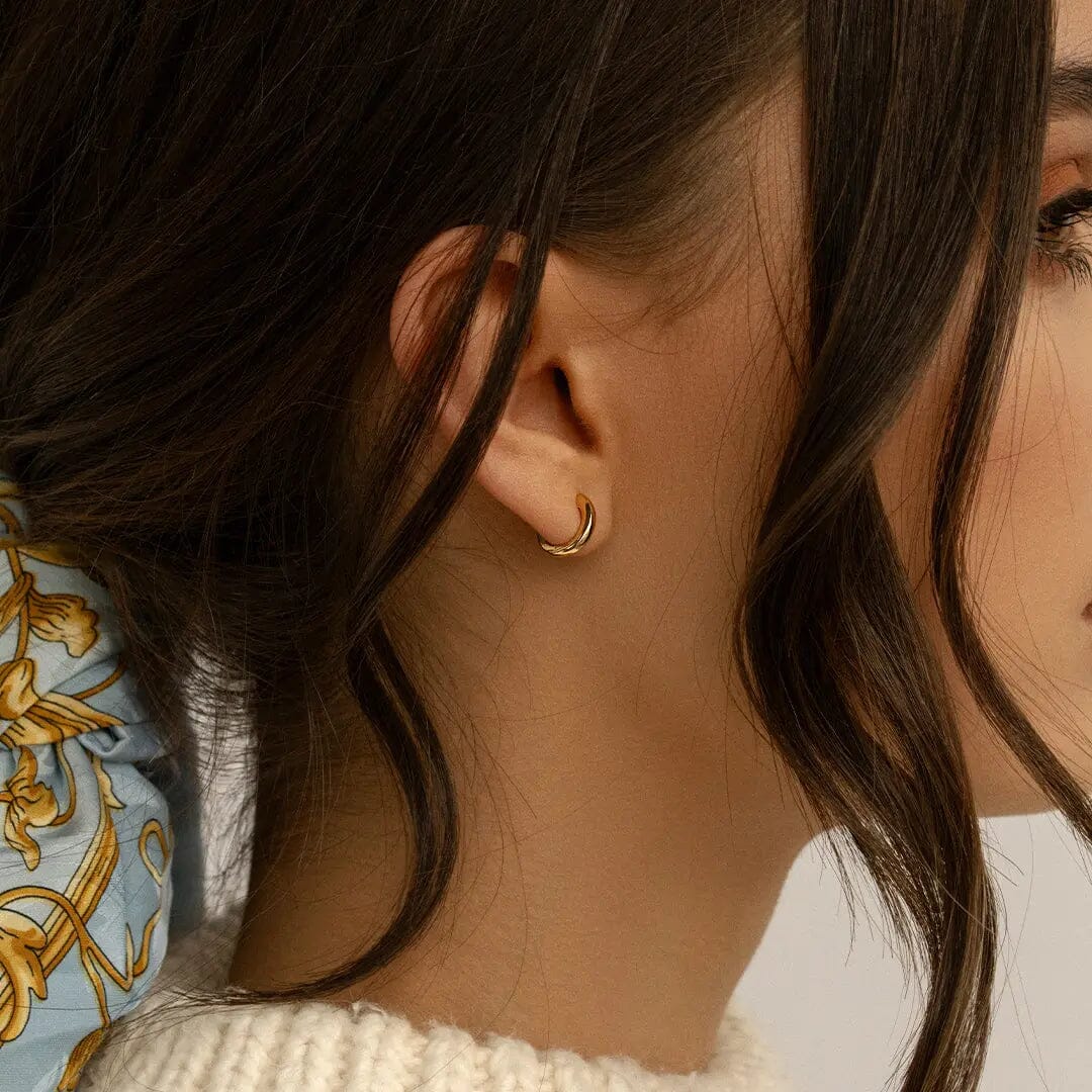 A gold huggie hoop earring., worn in models ear