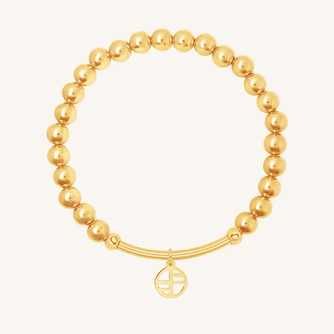 A gold-tone charm bracelet with a beaded design and a circular charm hanging from a bar.