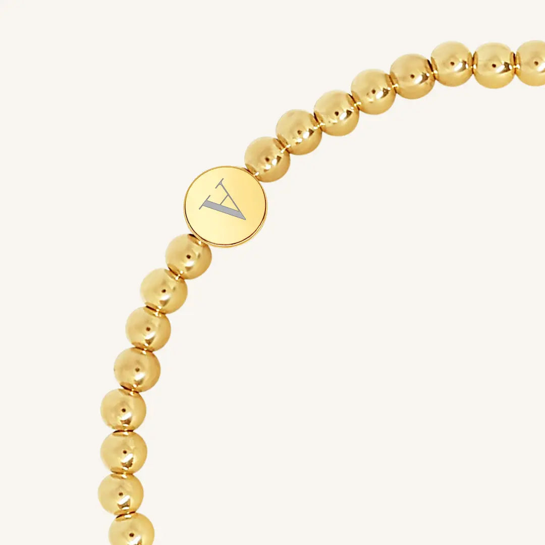 A gold bracelet with a beaded design and an engraveable bead, close up