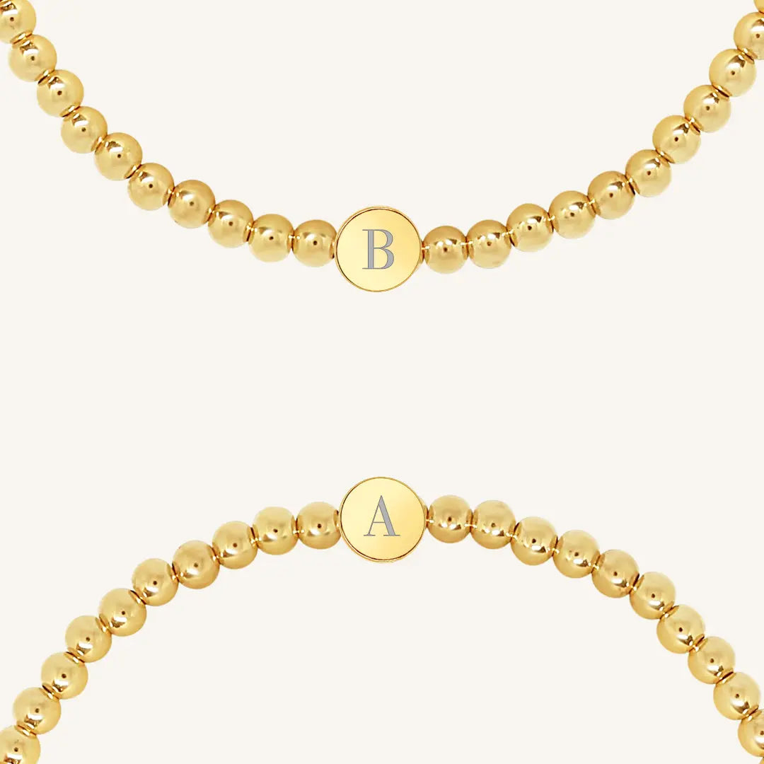 A gold bracelet with a beaded design and an engraveable bead, close up