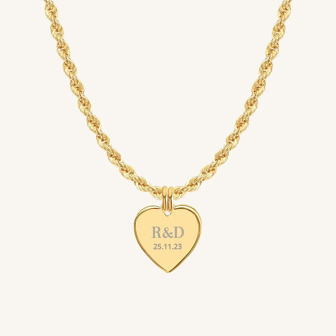 A gold heart-shaped necklace with a chain, featuring an engraved monogram initials and a date on the front.
