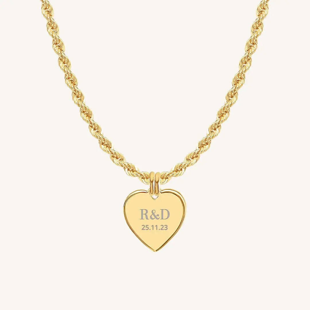 A gold heart-shaped necklace with a chain, featuring an engraved monogram initials and a date on the front.