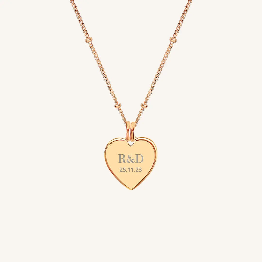A rose heart-shaped necklace with a chain, featuring an engraved monogram initials and a date on the front.