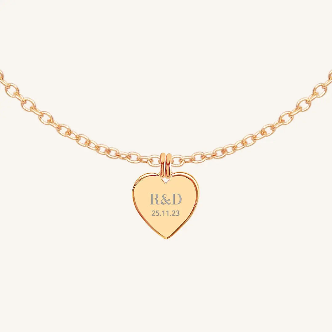 A rose heart-shaped necklace with a chain, featuring an engraved monogram initials and a date on the front.