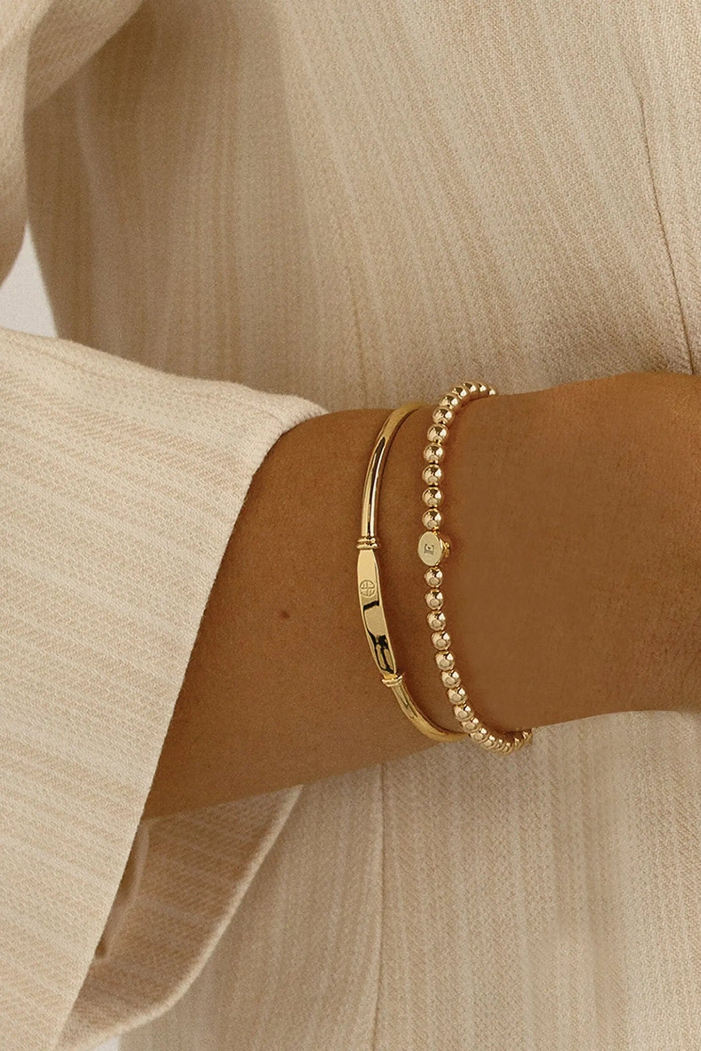 A gold bracelet with a beaded design and an engraveable bead, worn on models wrist