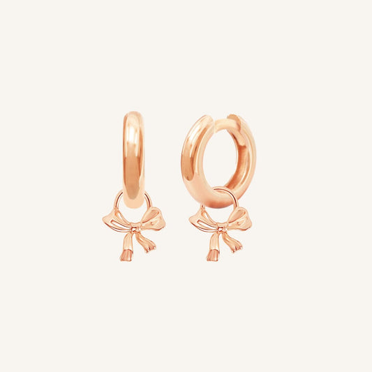 A pair of rose-colored hoop earrings with charm pendants attached to them, displayed against a white background.