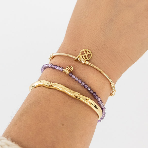 Gold and purple beaded bracelets on a wrist against a white background