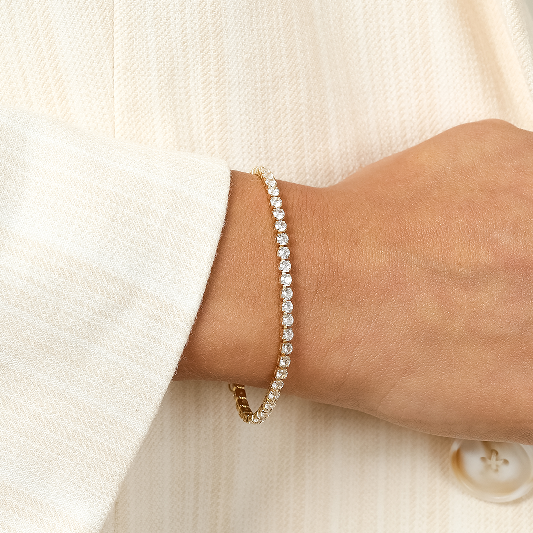 A gold-coloured tennis bracelet with clear cubic zirconias linked together, featuring a extender chain for adjustable length, close up on wrist