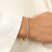 A gold-coloured tennis bracelet with clear cubic zirconias linked together, featuring a extender chain for adjustable length.