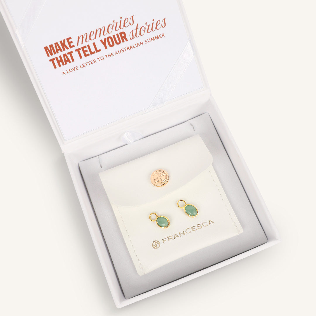 Gold hoop charms with green gemstones, displayed in white box
