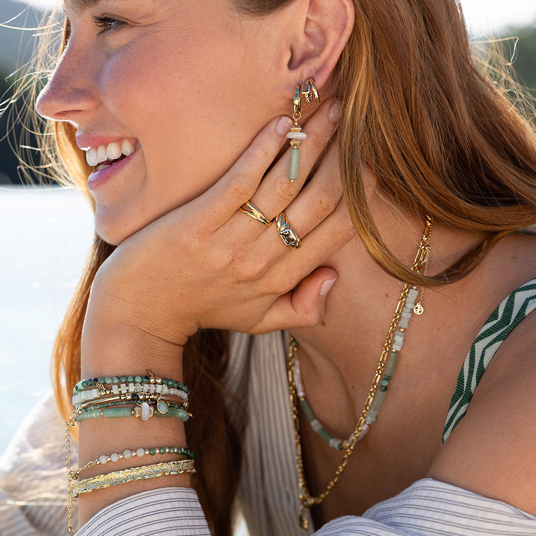 Woman wearing gold earrings and bracelets with a blurred background