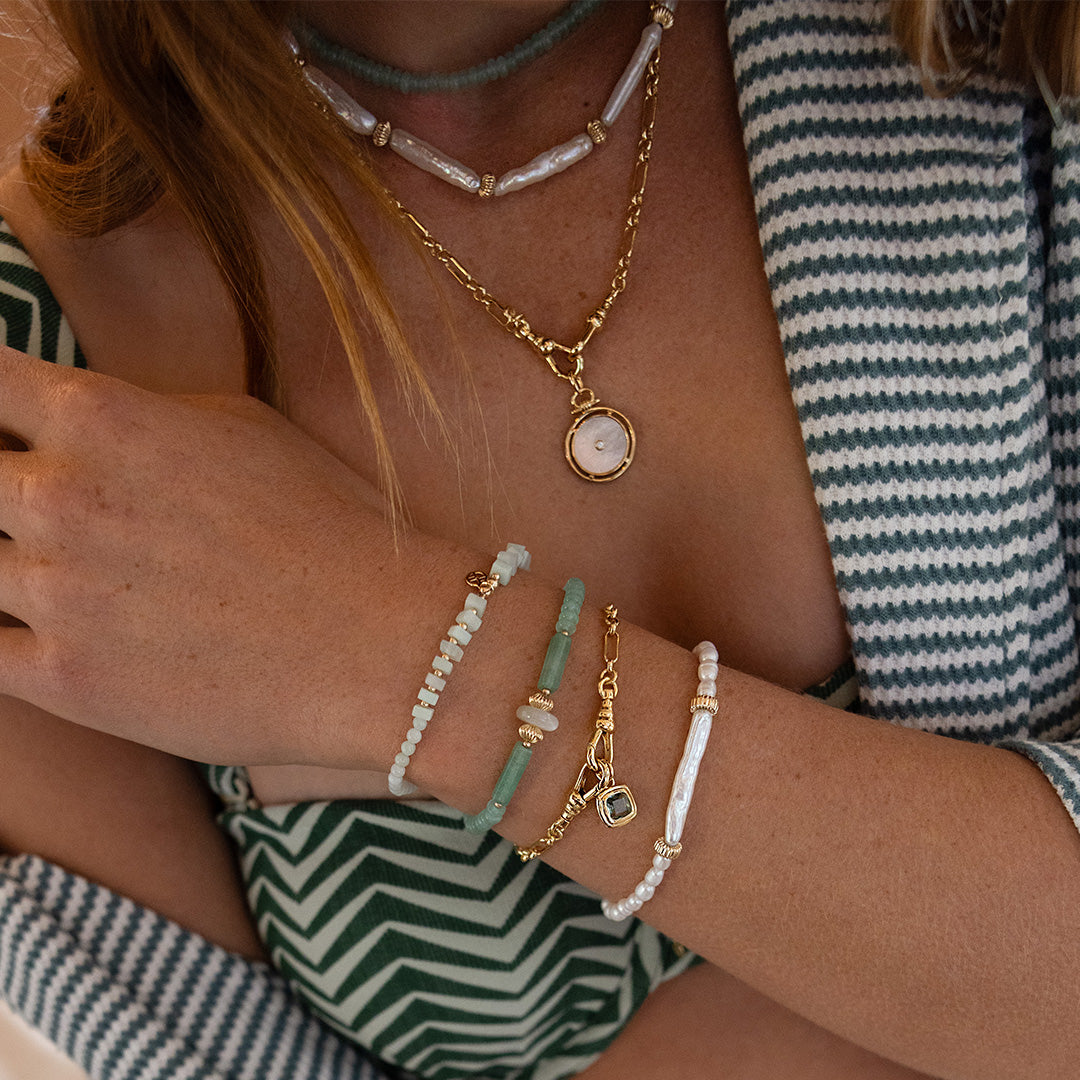 Close-up of a person wearing multiple necklaces and bracelets with a striped garment.