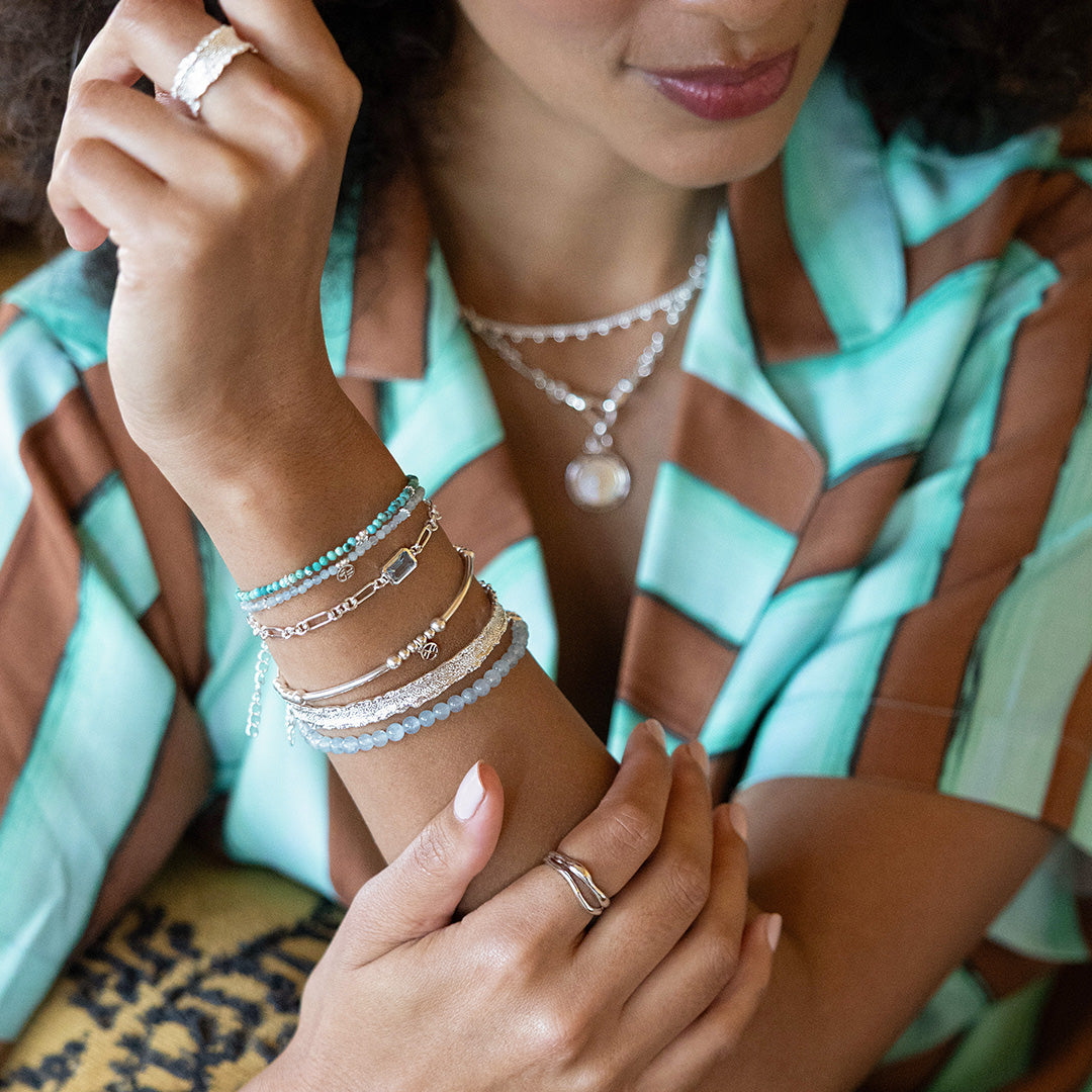 Close-up of a person's wrist with multiple bracelets and rings, wearing a patterned garment.