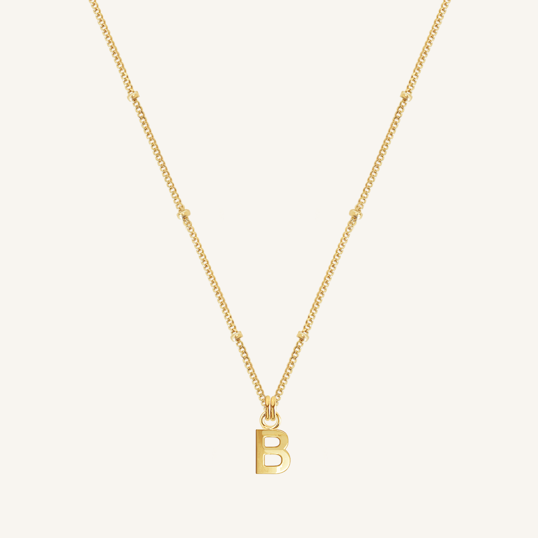 Gold necklace with a 'B' pendant on a light beige background