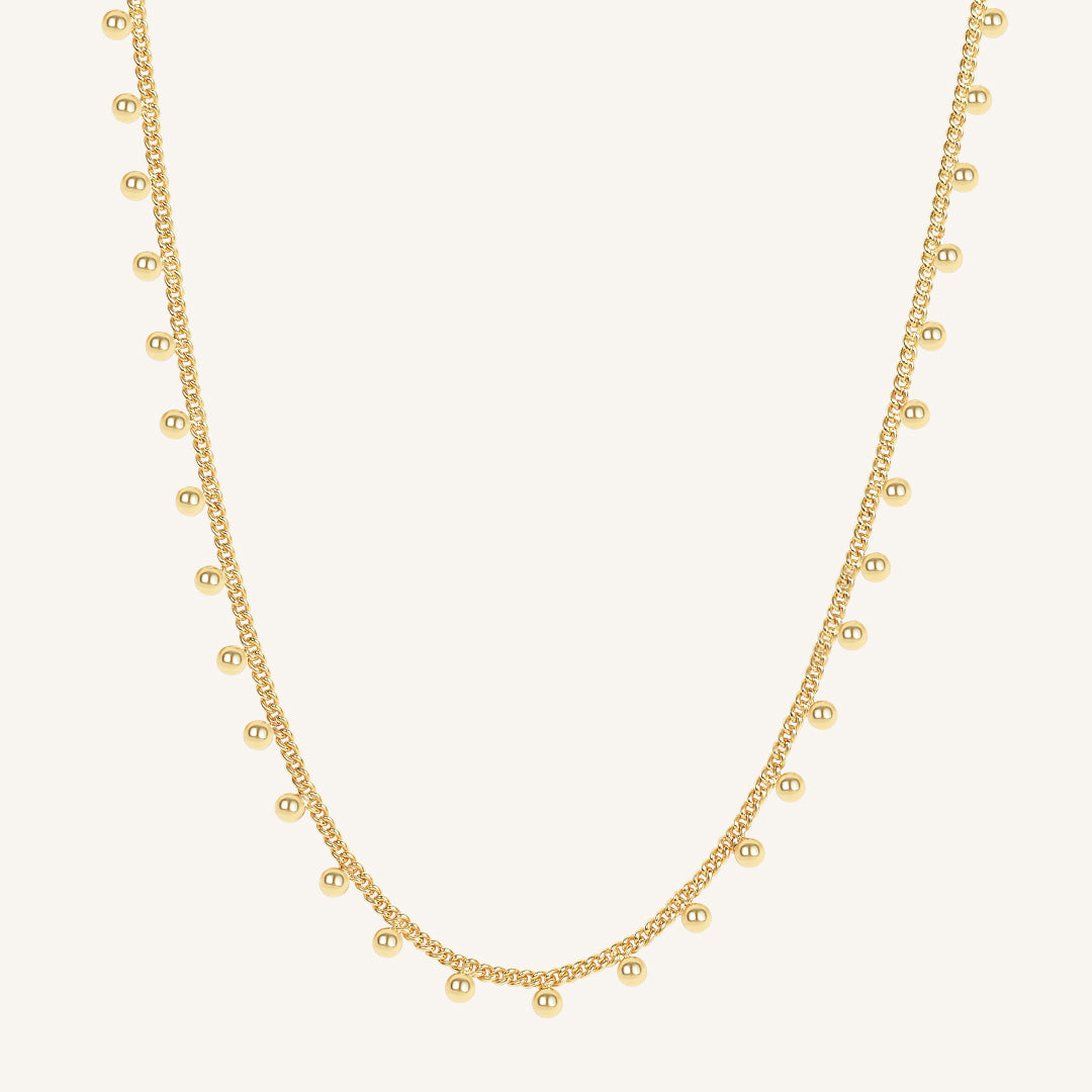 Gold necklace with small beads on a light beige background