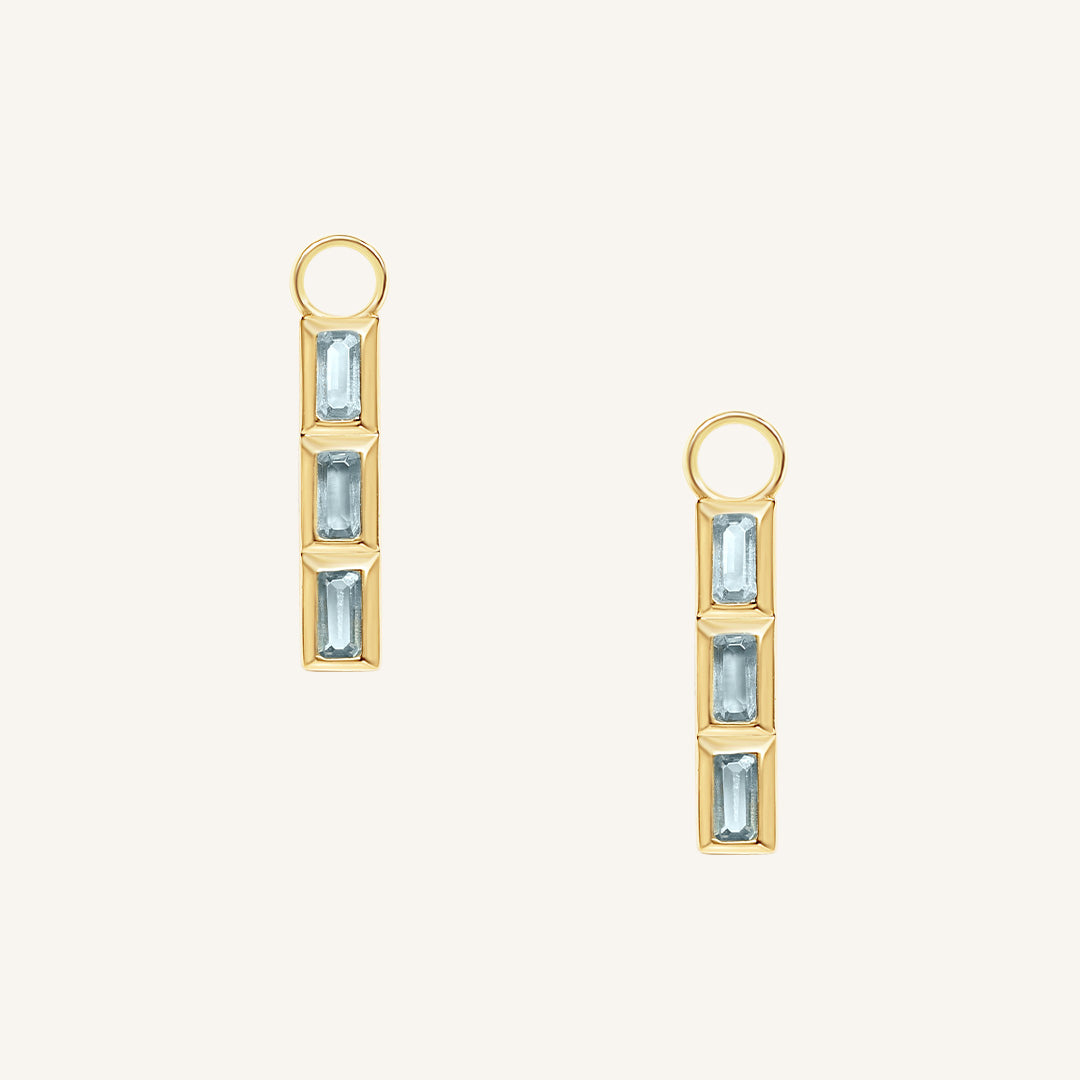 Gold hoop charms with blue gemstones on a white background
