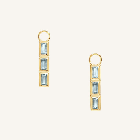 Gold hoop charms with blue gemstones on a white background