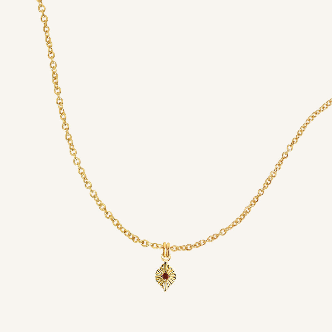 Gold necklace with a small pendant on a light beige background