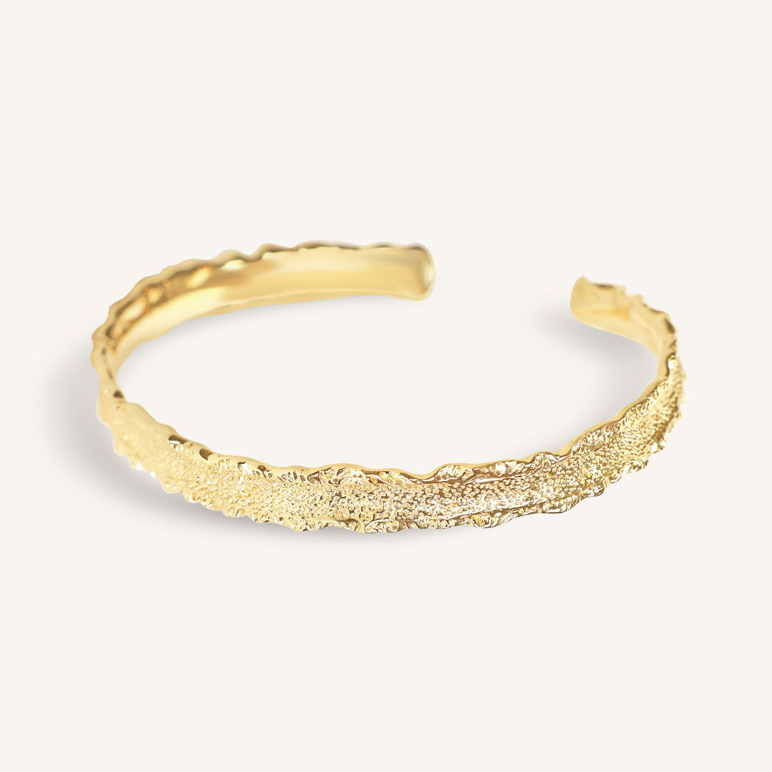 Gold cuff with textured design on a light gray background