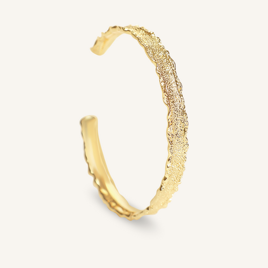 Gold cuff with textured design on a light gray background