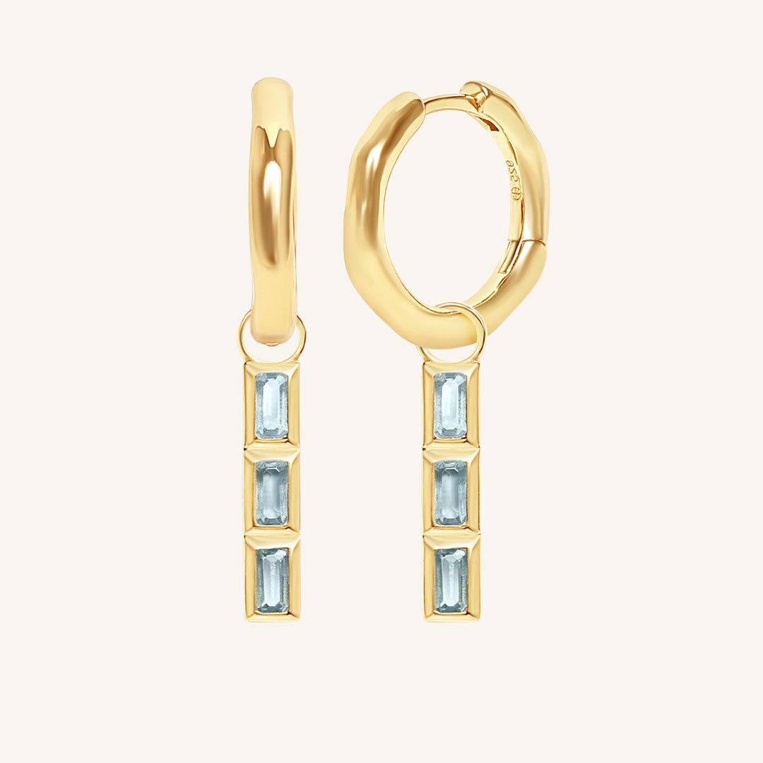 Gold hoop earrings with blue gemstones on a white background