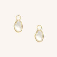 Gold hoop charms with white stones on a light beige background