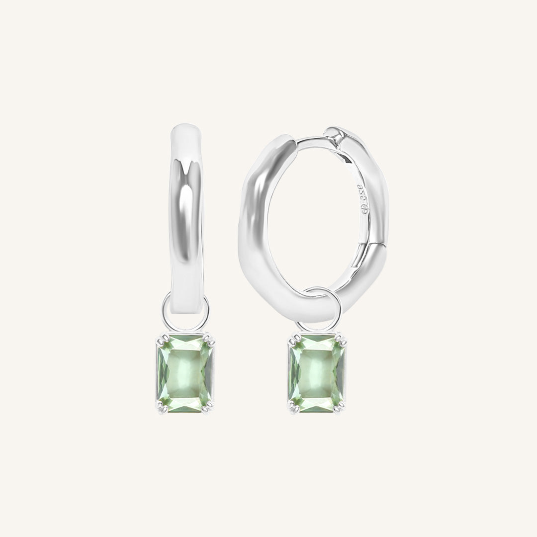 Silver hoop earrings with green gemstones on a white background