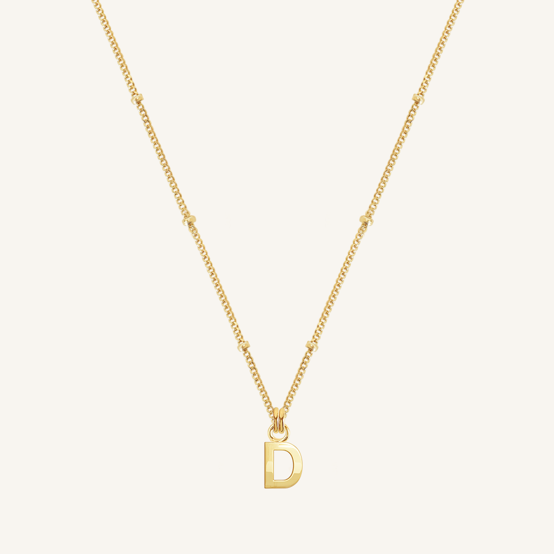 Gold necklace with a 'D' pendant on a light beige background