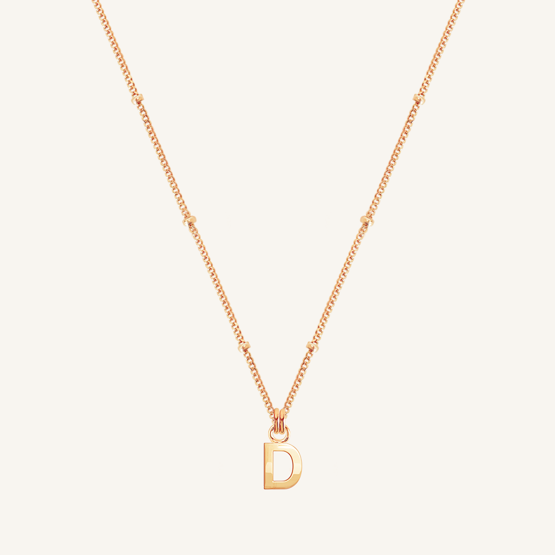 Gold necklace with a 'D' pendant on a light beige background