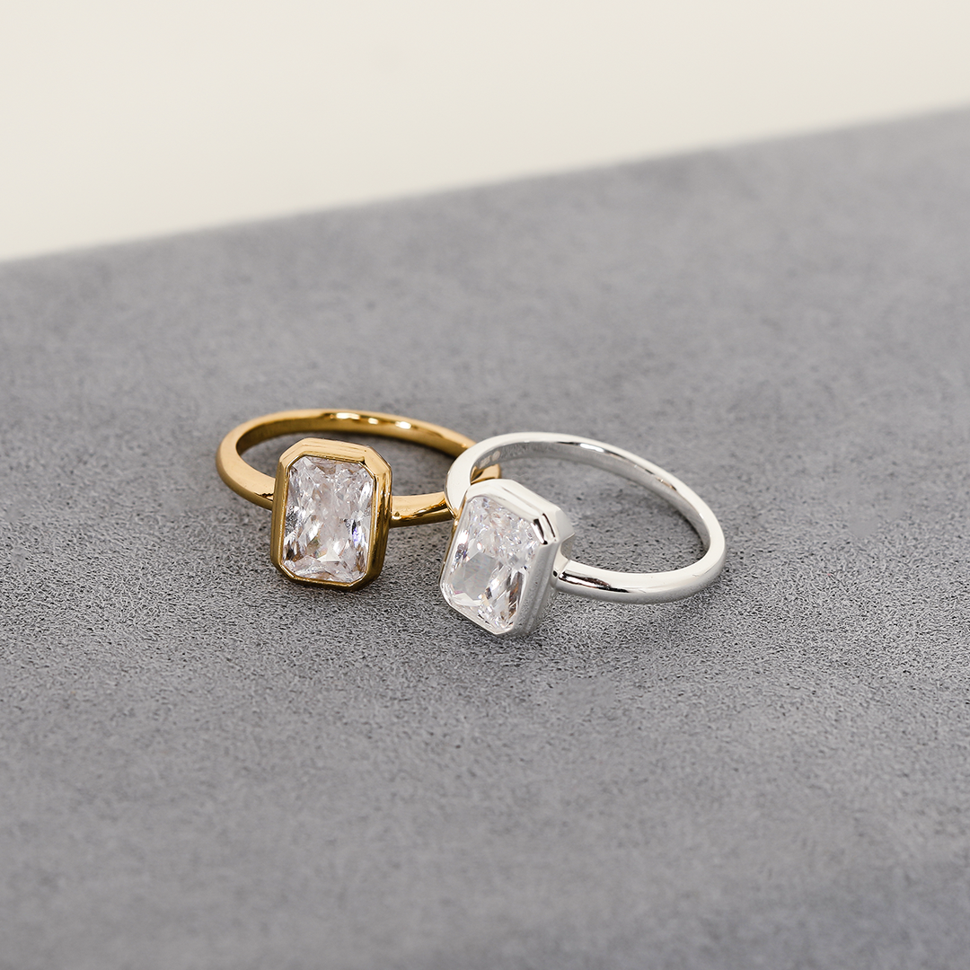 A gold-coloured and silver-coloured ring with a white cubic zirconia, bezel set in a rectangular frame with a smooth, polished band.
