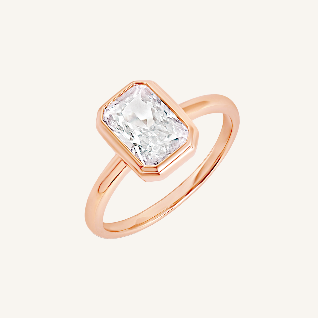 A rose gold-coloured ring with a white cubic zirconia, bezel set in a rectangular frame with a smooth, polished band.