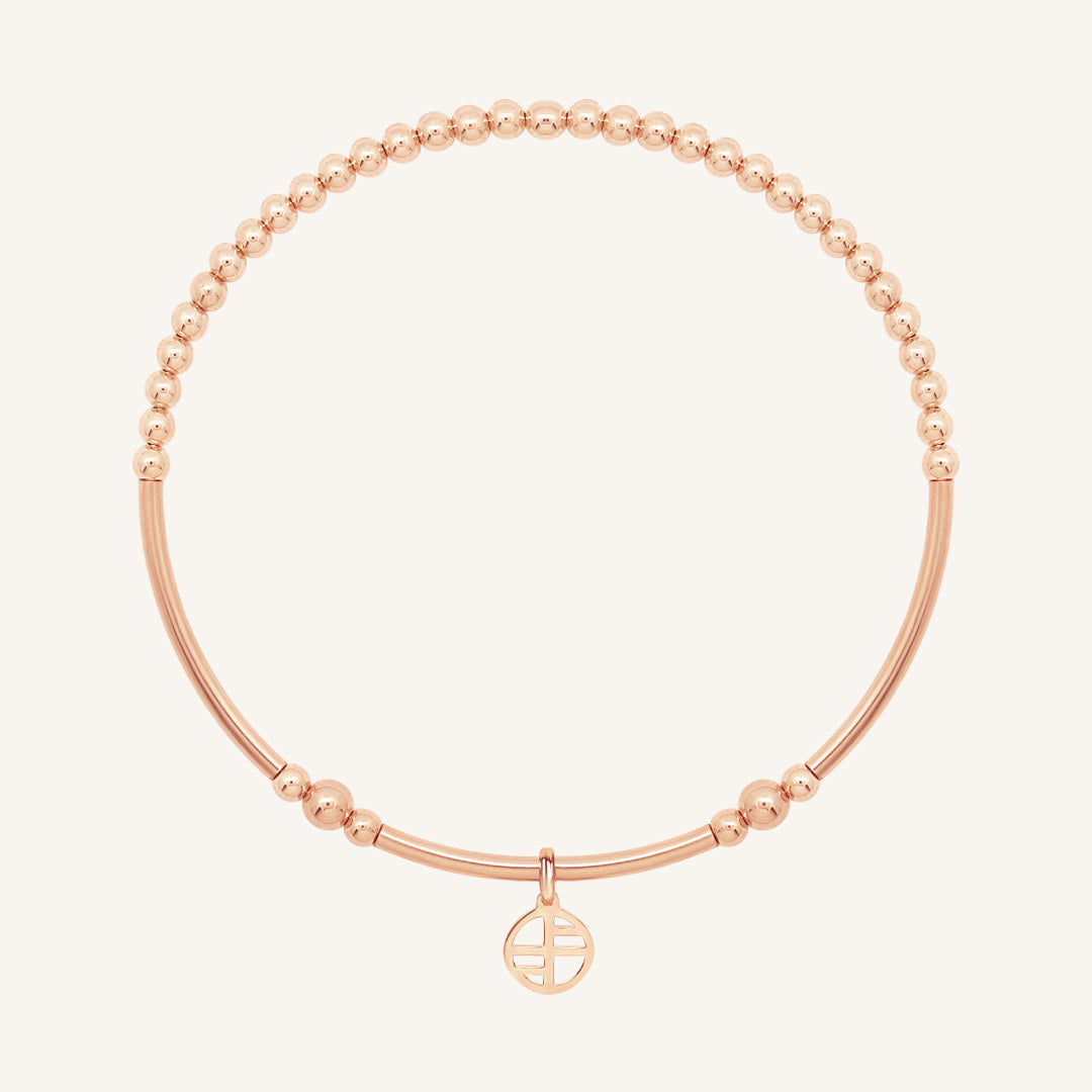 Rose gold bracelet with a small charm on a white background