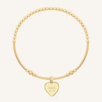 A gold bracelet with a beaded design and a heart-shaped charm, engraved with initials and a date 