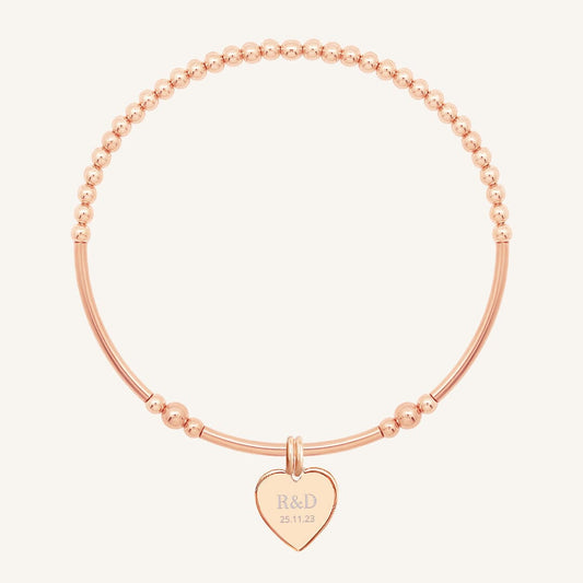 A rose bracelet with a beaded design and a heart-shaped charm, engraved with initials and a date 