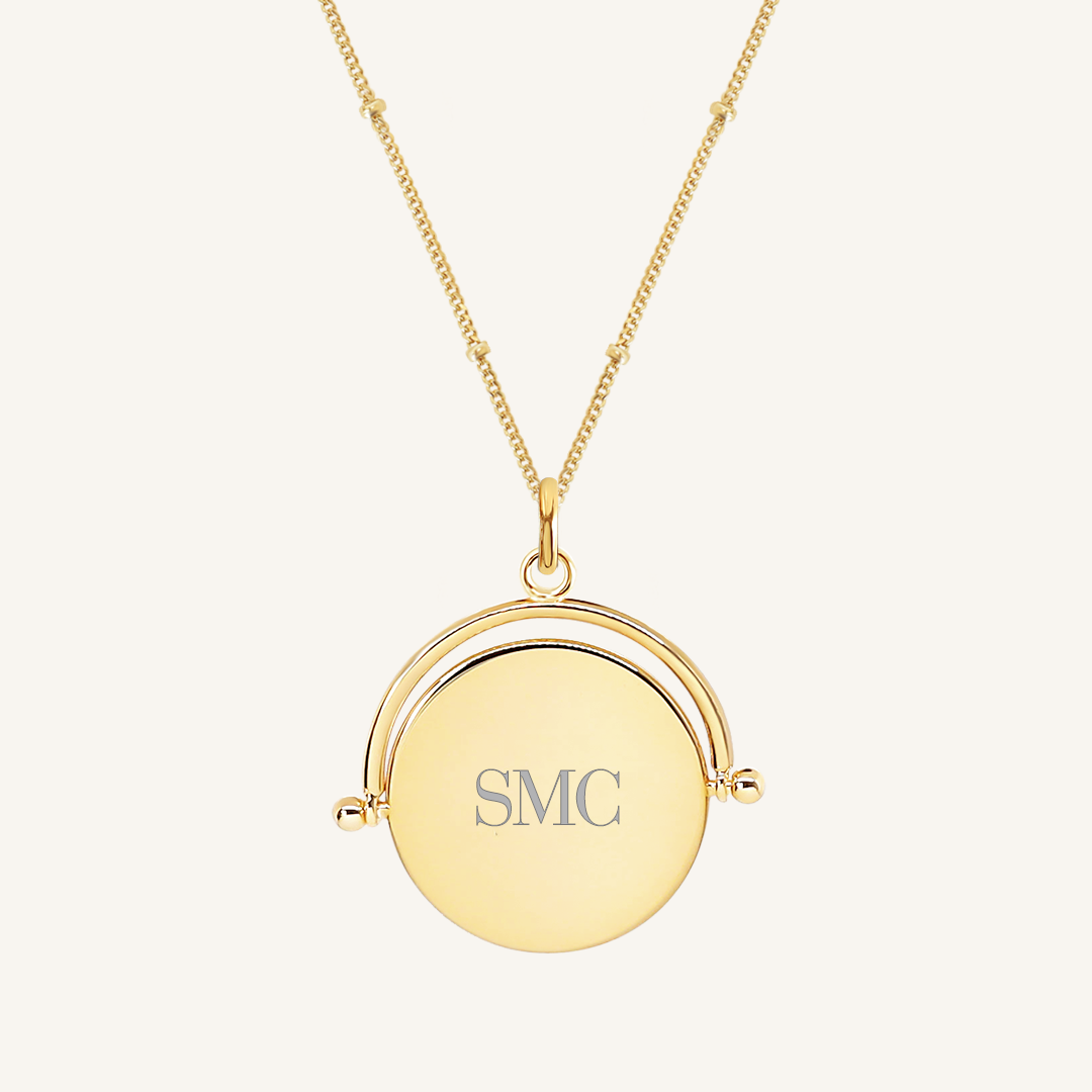 A gold-coloured pendant with the initials  engraved on it, featuring a spinning mechanism, on gold chain
