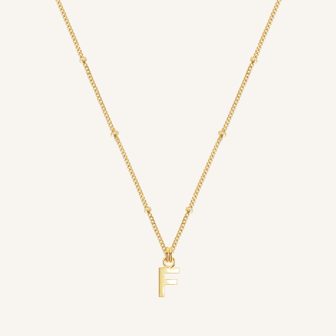 Gold necklace with a 'F' pendant on a light beige background