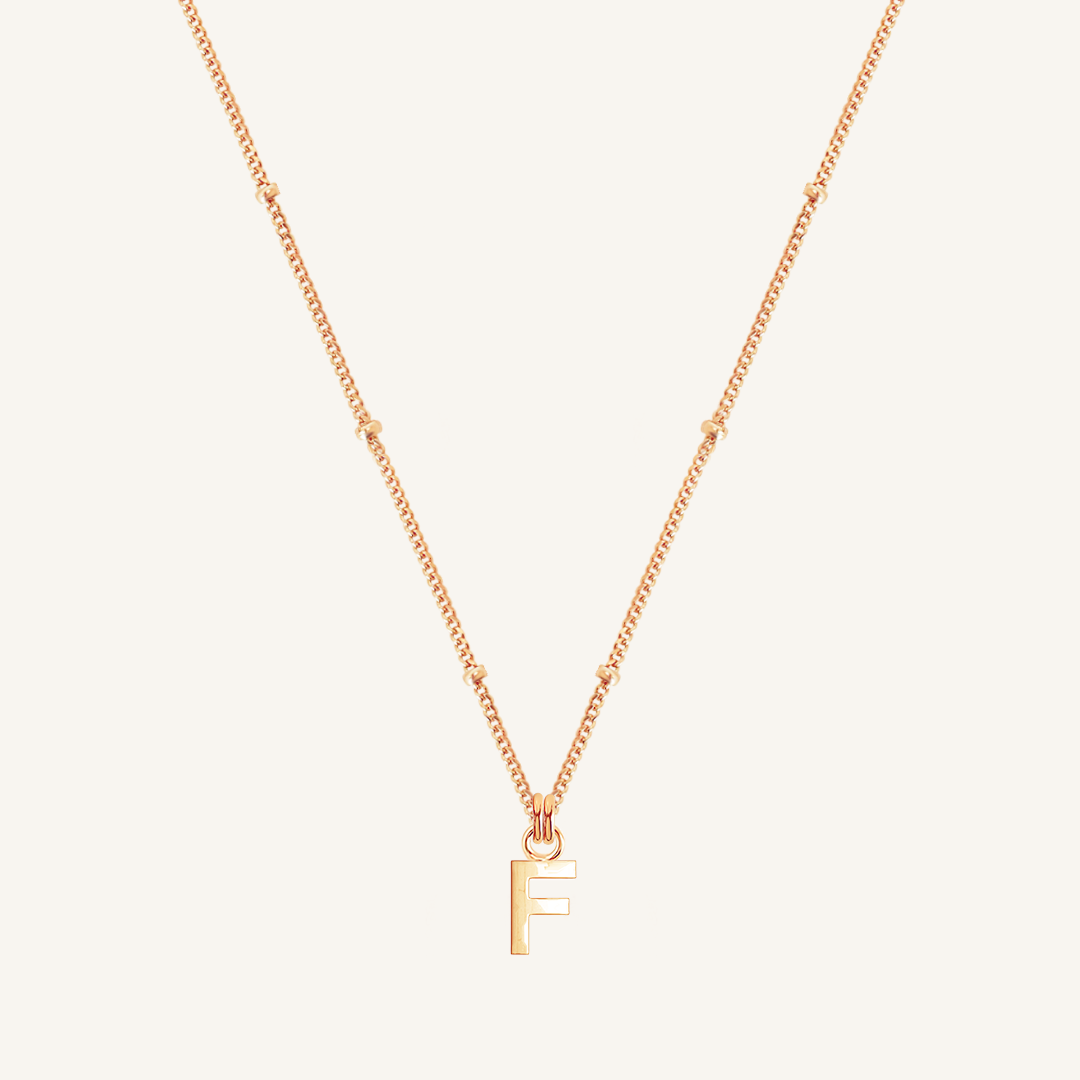Gold necklace with a 'F' pendant on a light beige background