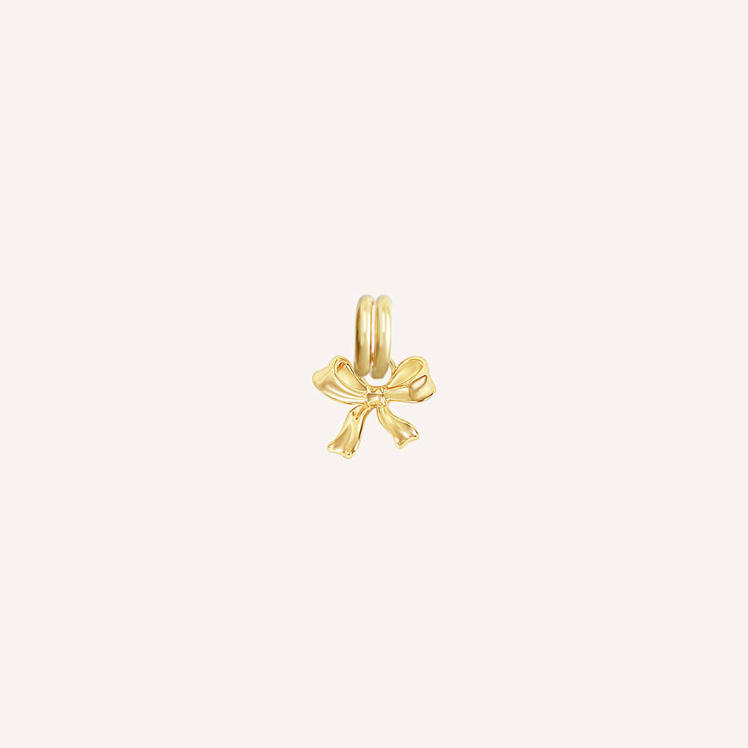 A small gold bow charm with a loop on top for attachment, displayed on a white background.