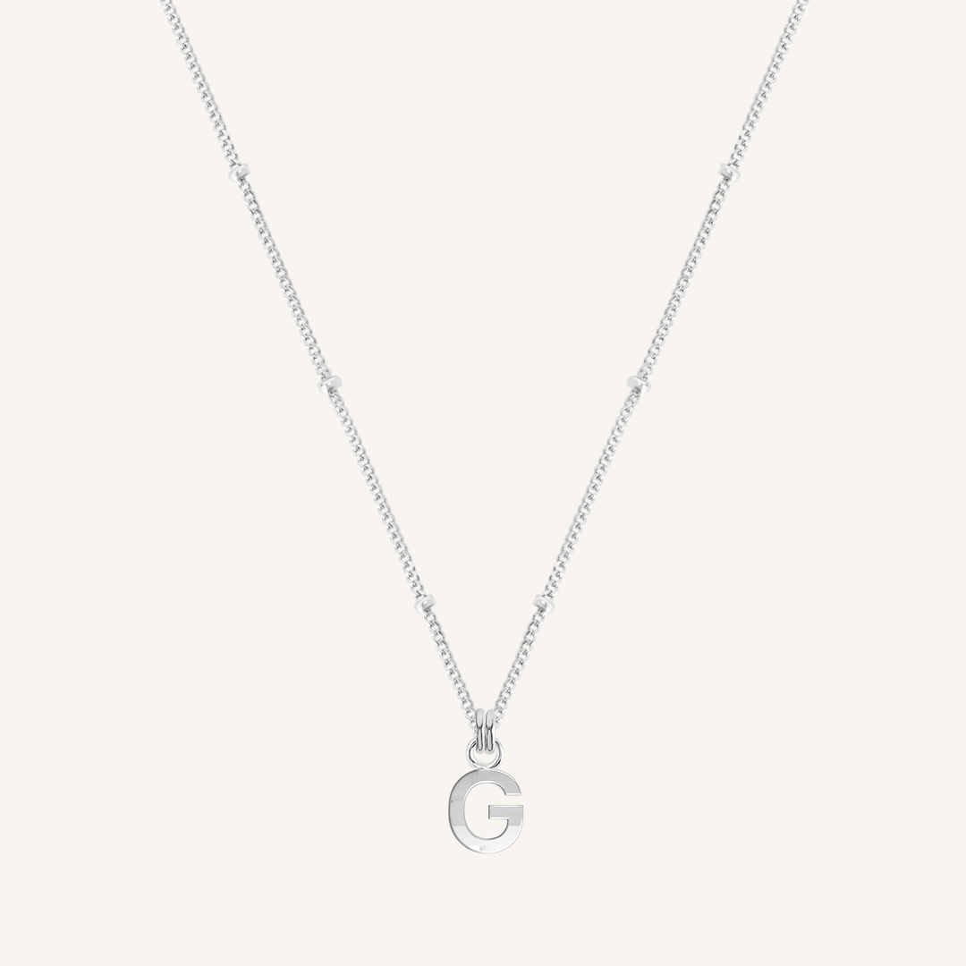 Silver necklace with a letter 'G' pendant on a light gray background