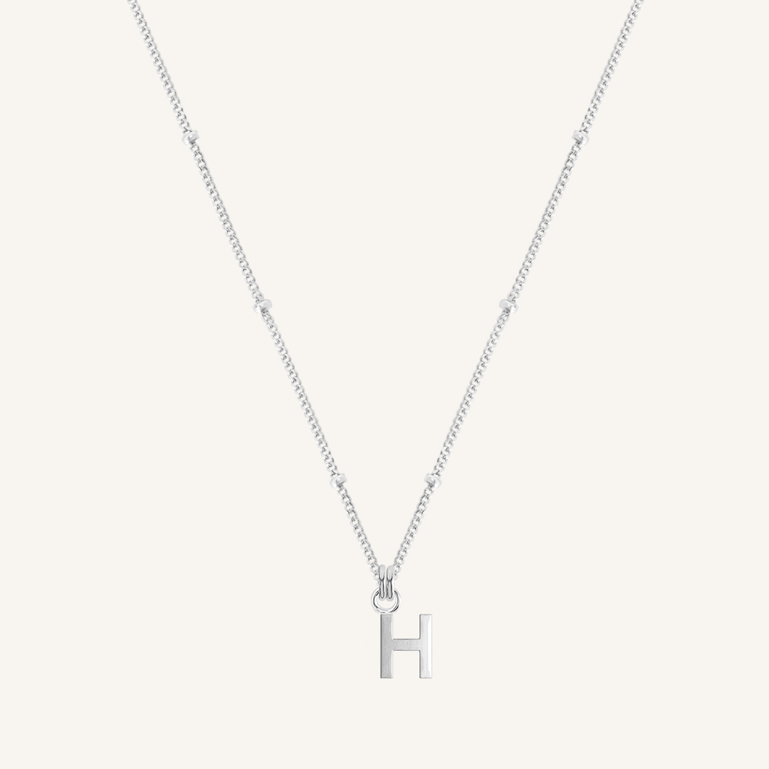 Silver necklace with a 'H' pendant on a light gray background