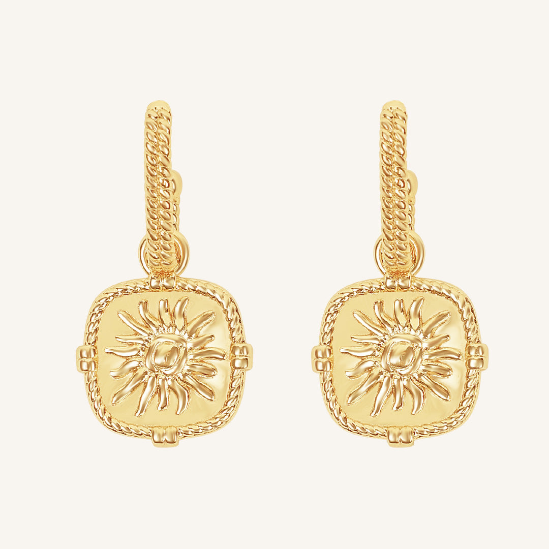 Gold earrings with sun design on a white background