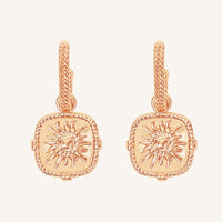 Rose gold earrings with sun design on a light pink background
